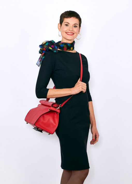 femme de 3/4 face portant une robe noire, col bateau couvrant les clavicules, manches 3/4, avec autour du cou un foulard fond noir et un sac rouge en bandoulière