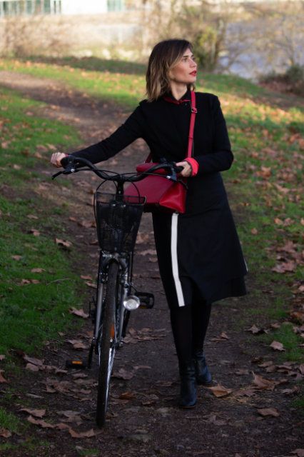 sur-jupe de protection pluie, noire avec une large bande réfléchissante verticale pour la visibilité, portée par une cycliste poussant son vélo