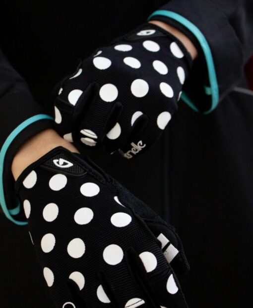 mains de femme portant des gants noirs à pois blancs, logo Giro au poignet et marque Cyclamelle sur le petit doigt