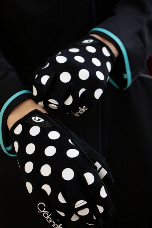 mains de femme portant des gants noirs à pois blancs, logo Giro au poignet et marque Cyclamelle sur le petit doigt