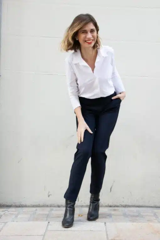 pantalon porté par une femme penchée vers l'avant, genoux pliés, chemisier blanc col ouvert porté manche 3/4 d'un côté, manche longue de l'autre